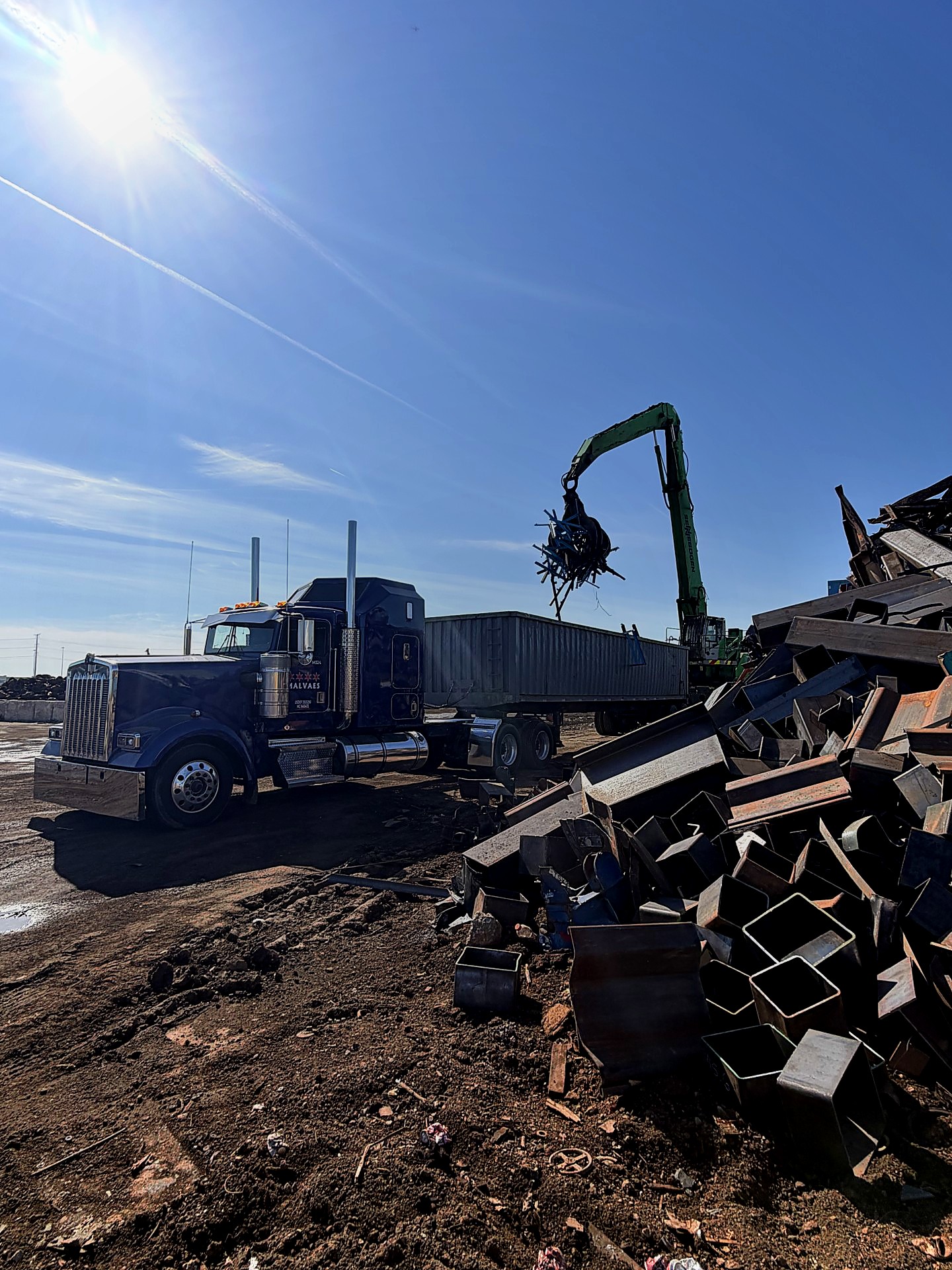 A Malvaes Kenworth truck and trailer at a metal recycling yard with a grapple crane handling scrap metal